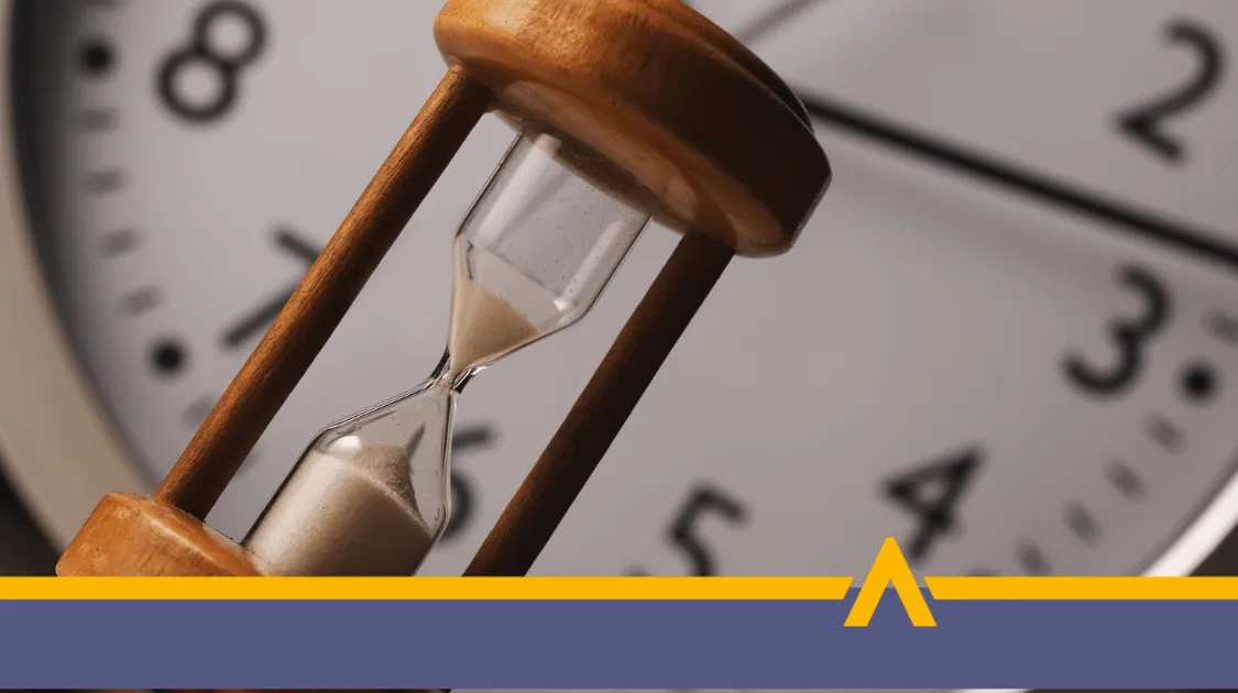 Klepsydra z przesypującym się piaskiem na tle dużej tarczy zegara