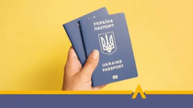 Dłoń trzymająca dwa niebieskie paszporty Ukrainy na żółtym tle.